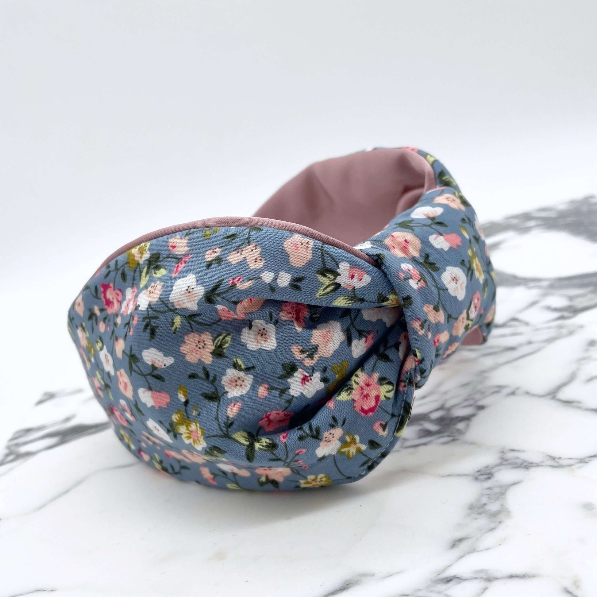 A pink, blue and white ditsy print knot-style headband on a marble slab.