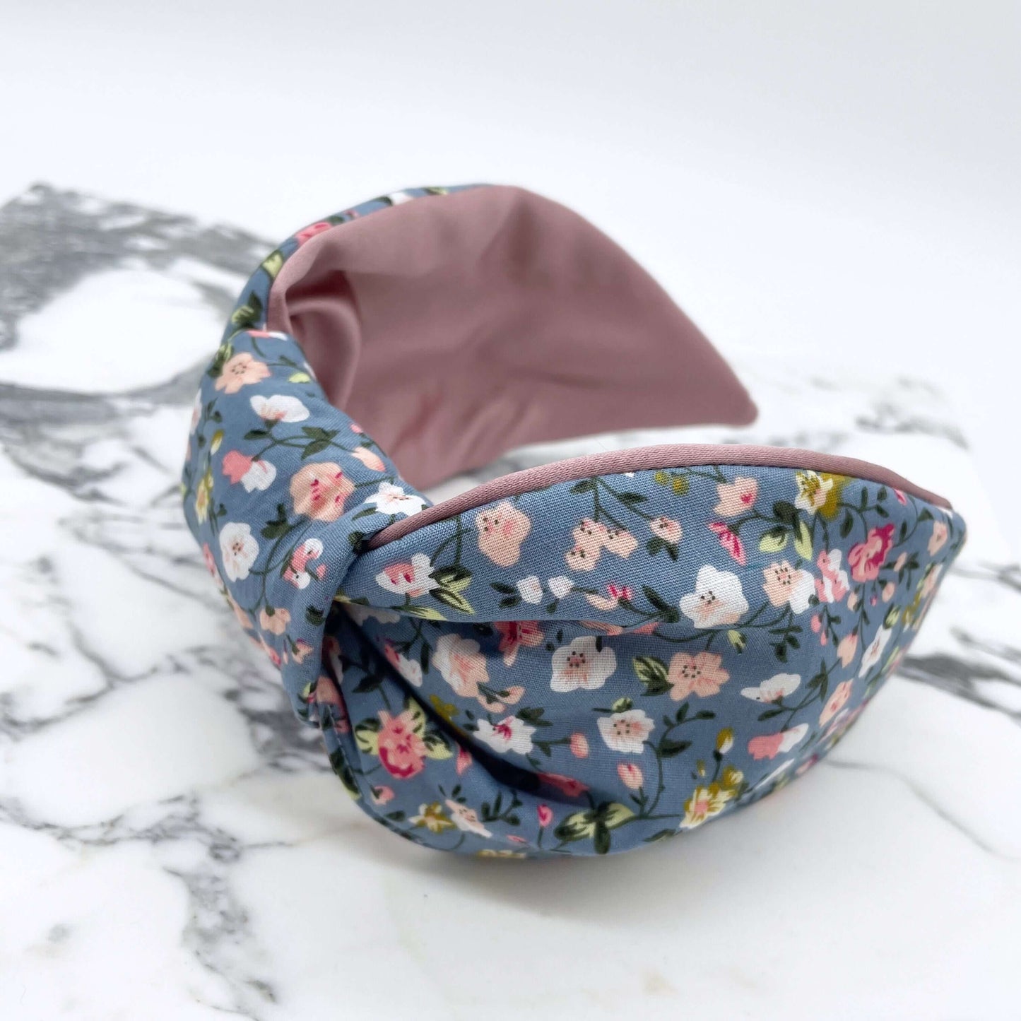A pink, blue and white ditsy print knot-style headband on a marble slab.