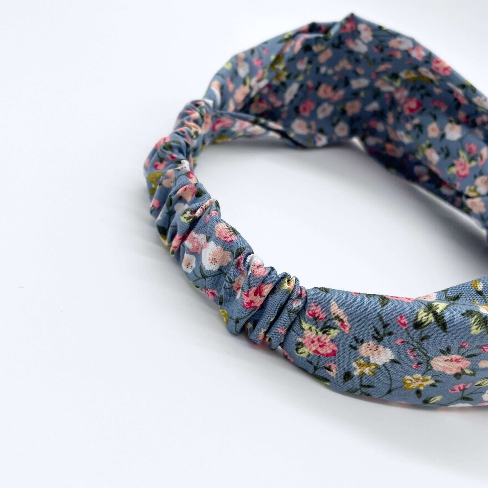 A pink, blue and white ditsy print elasticated cotton headband on a white background.
