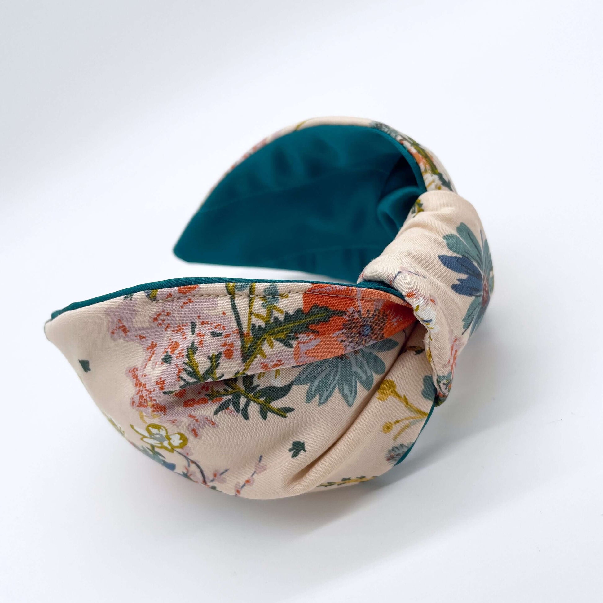 A cream floral knotted headband with a teal satin lining on a white background