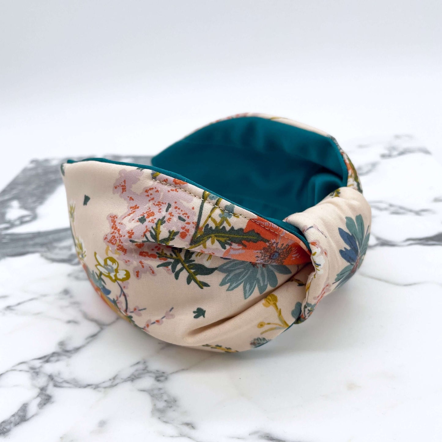 A cream floral knotted headband with a teal satin lining on a marble slab.