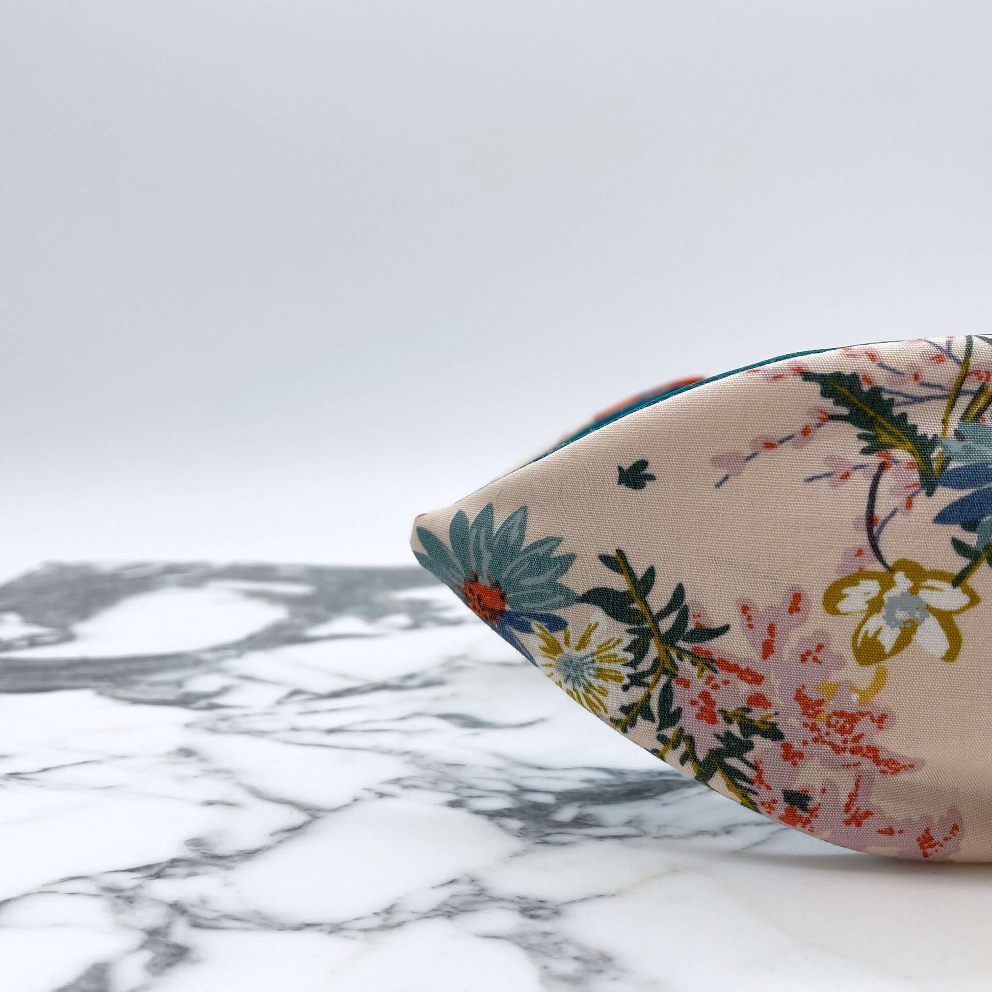 A cream floral knotted headband with a teal satin lining on a marble slab.