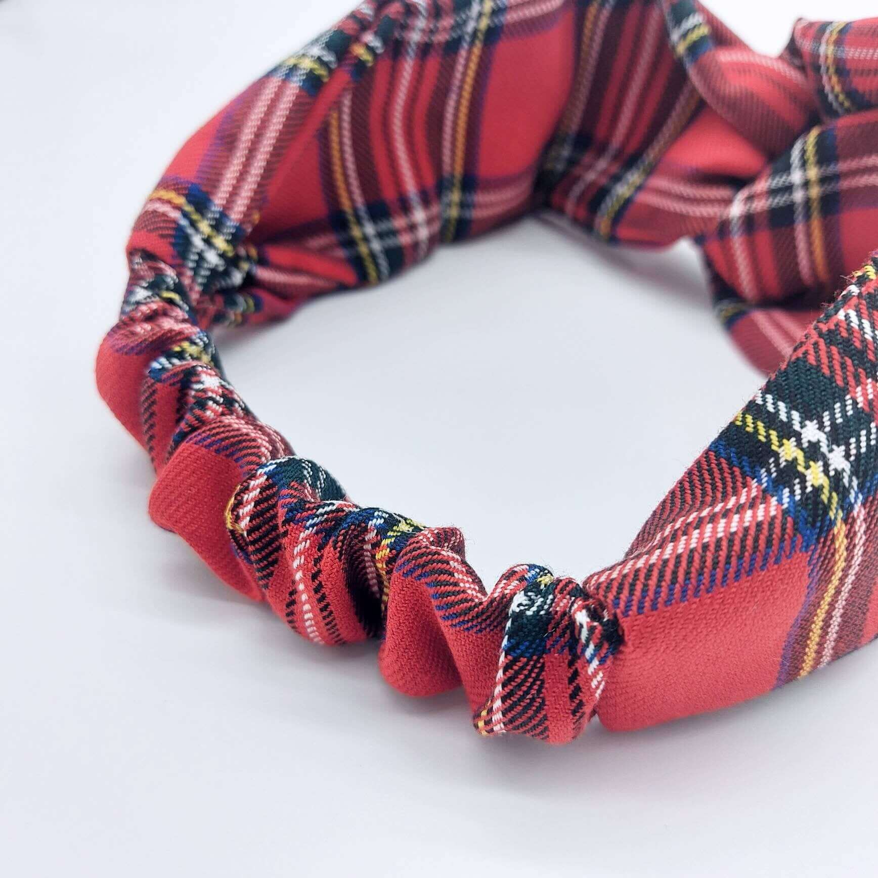 A soft, red traditional tartan, plaid, check, elasticated fabric headband, with a turban twist design at the front.