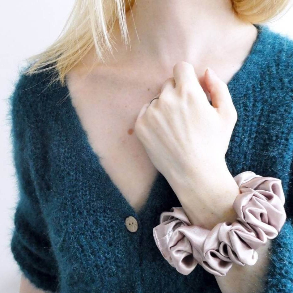 Model wearing a rose coloured, large, luxury satin hair scrunchie around the wrist.