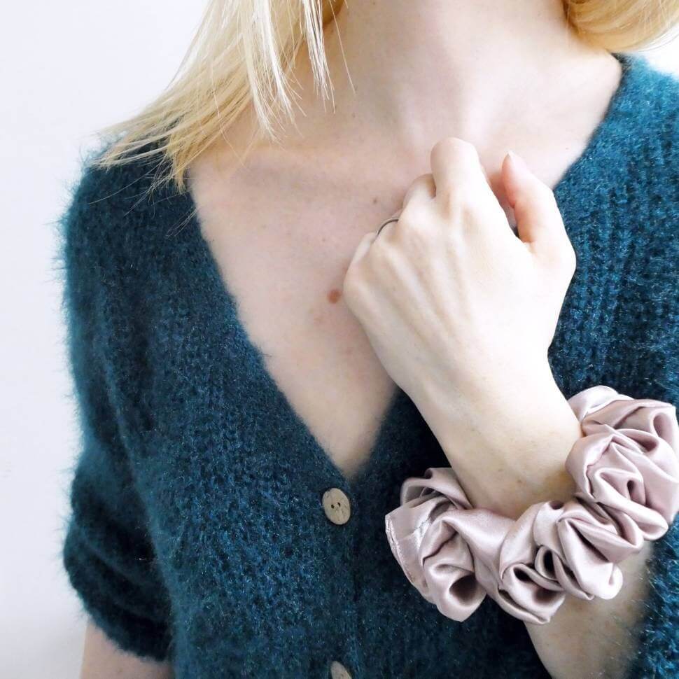 Model wearing a rose coloured, large, luxury satin hair scrunchie around the wrist