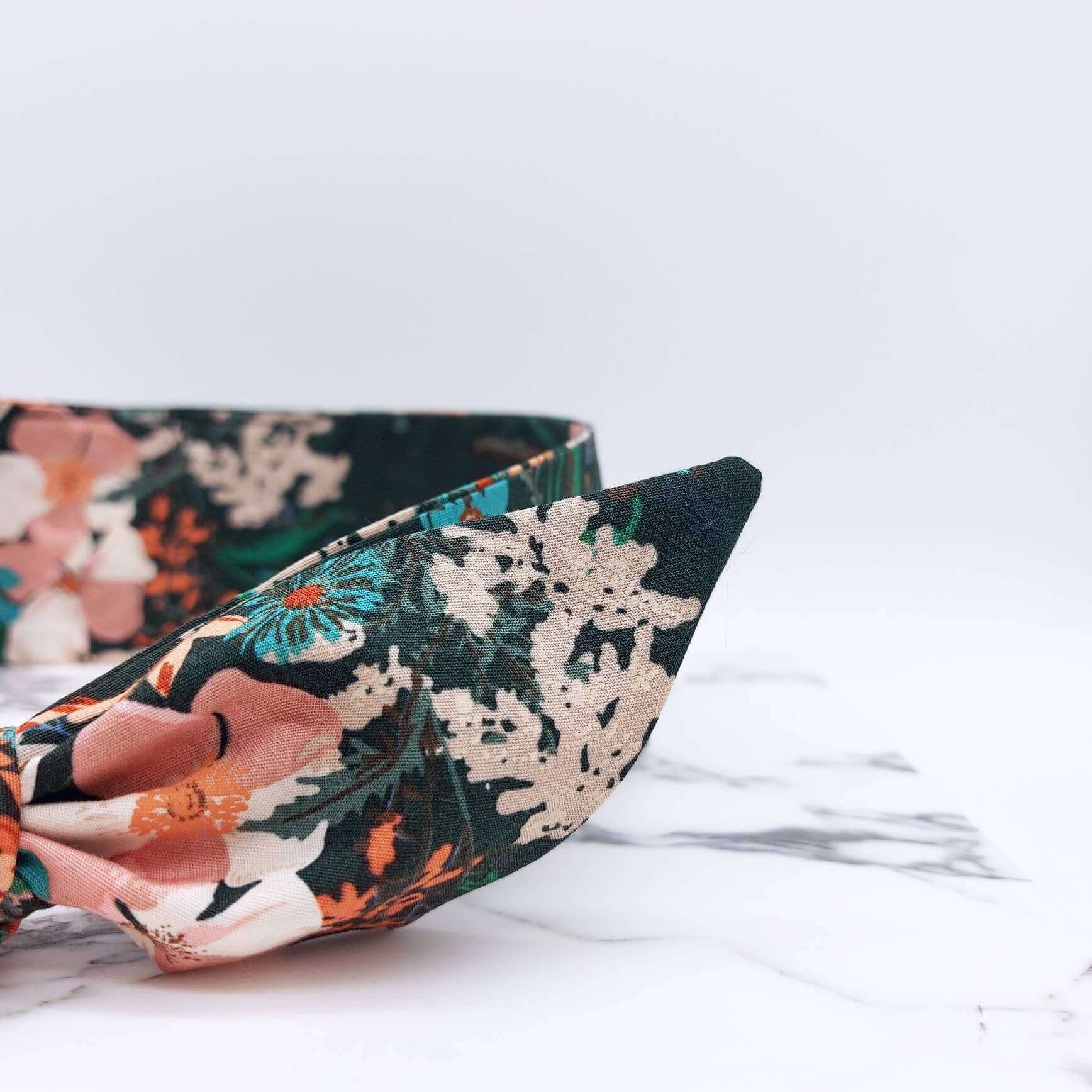 A dark green, floral cotton headscarf with pale pink, blue and orange flowers, tied in a pretty knot.