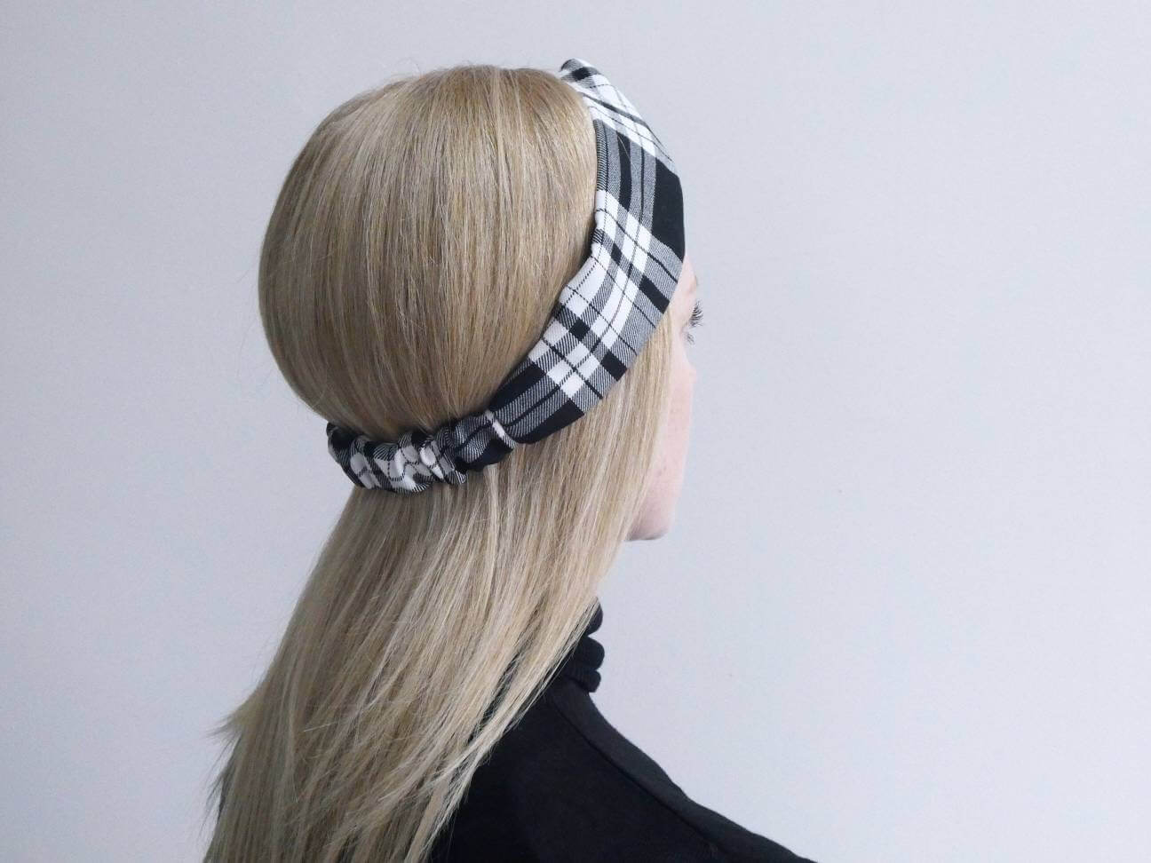 A model wears a soft, black and white tartan plaid check, turban twist headband with an elasticated panel at the back.