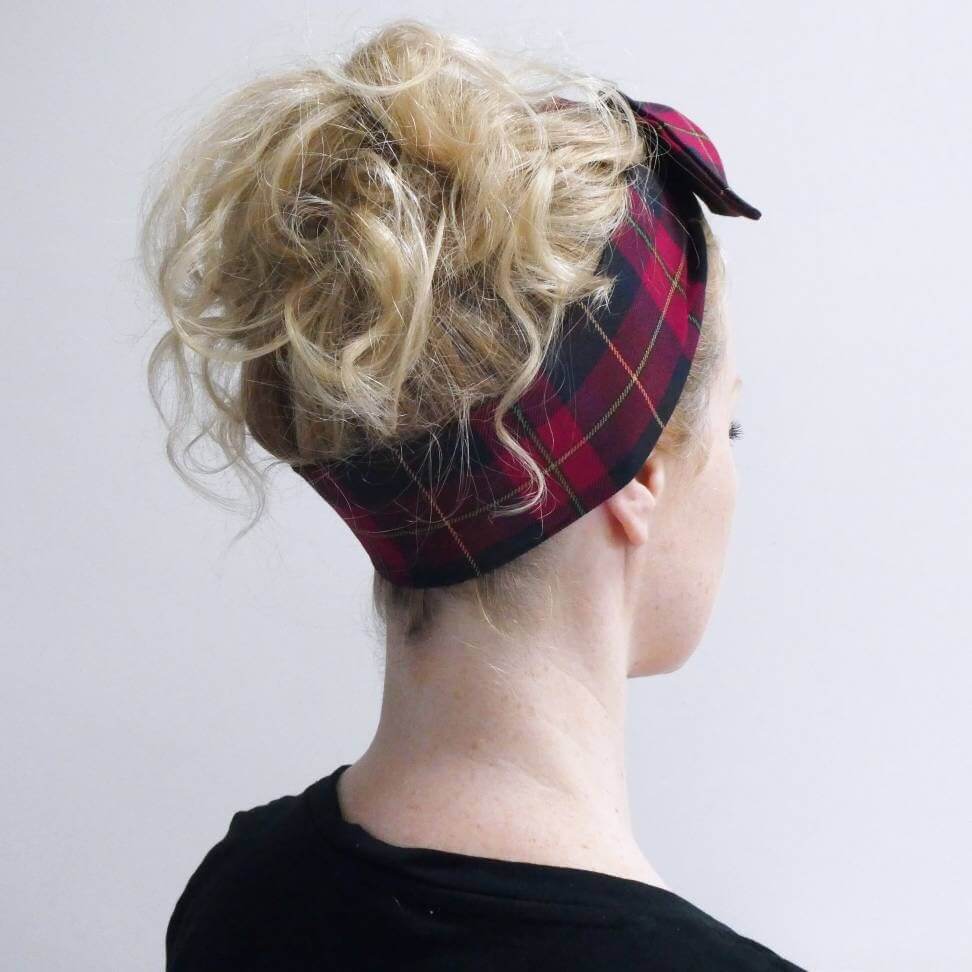 Model wears a dark cranberry and brown fabric, tartan paid tie headscarf, tied in a pretty knot.