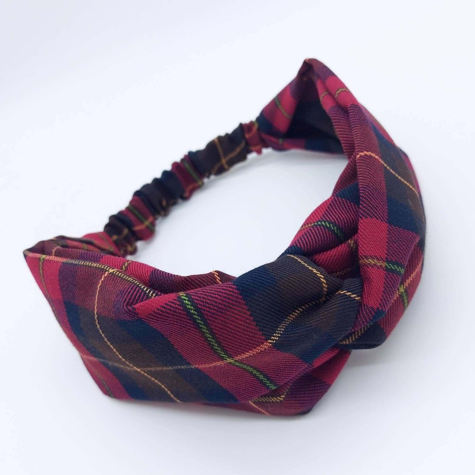A soft, cranberry red, tartan, plaid, check, elasticated fabric headband, with a turban twist design at the front.
