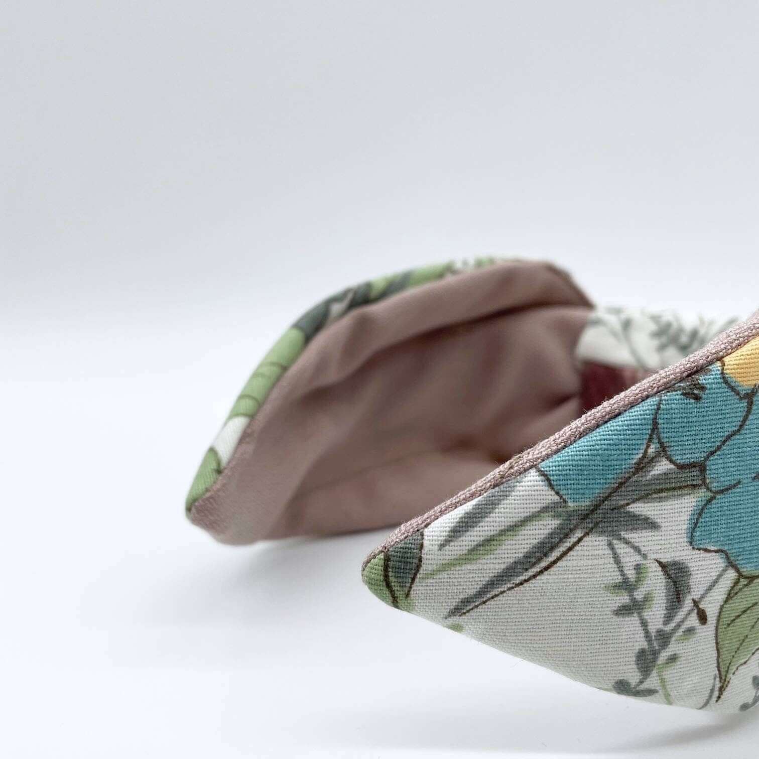 A bow-style, cream fabric headband with large pastel flowers with a soft pink lining underneath.
