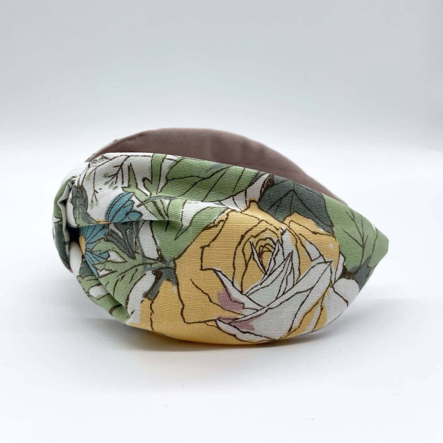 A bow-style, cream fabric headband with large pastel flowers with a soft pink lining underneath.