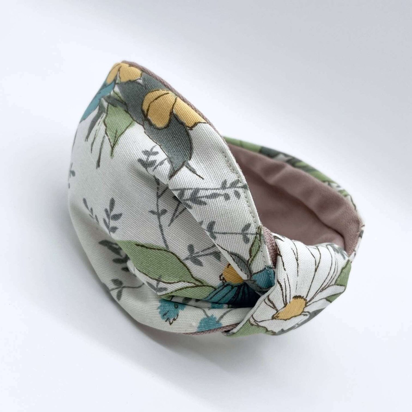 A bow-style, cream fabric headband with large pastel flowers with a soft pink lining underneath.
