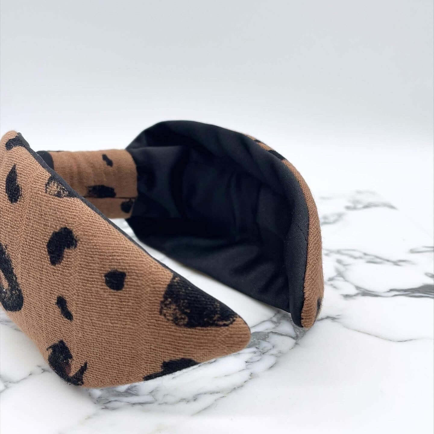 A luxury bow-style, brown and black animal print, fabric knot headband with a soft black lining underneath.