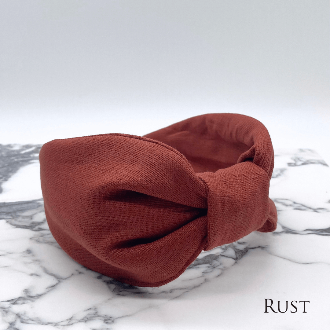 A rust linen knotted headband sitting on a marble tile.