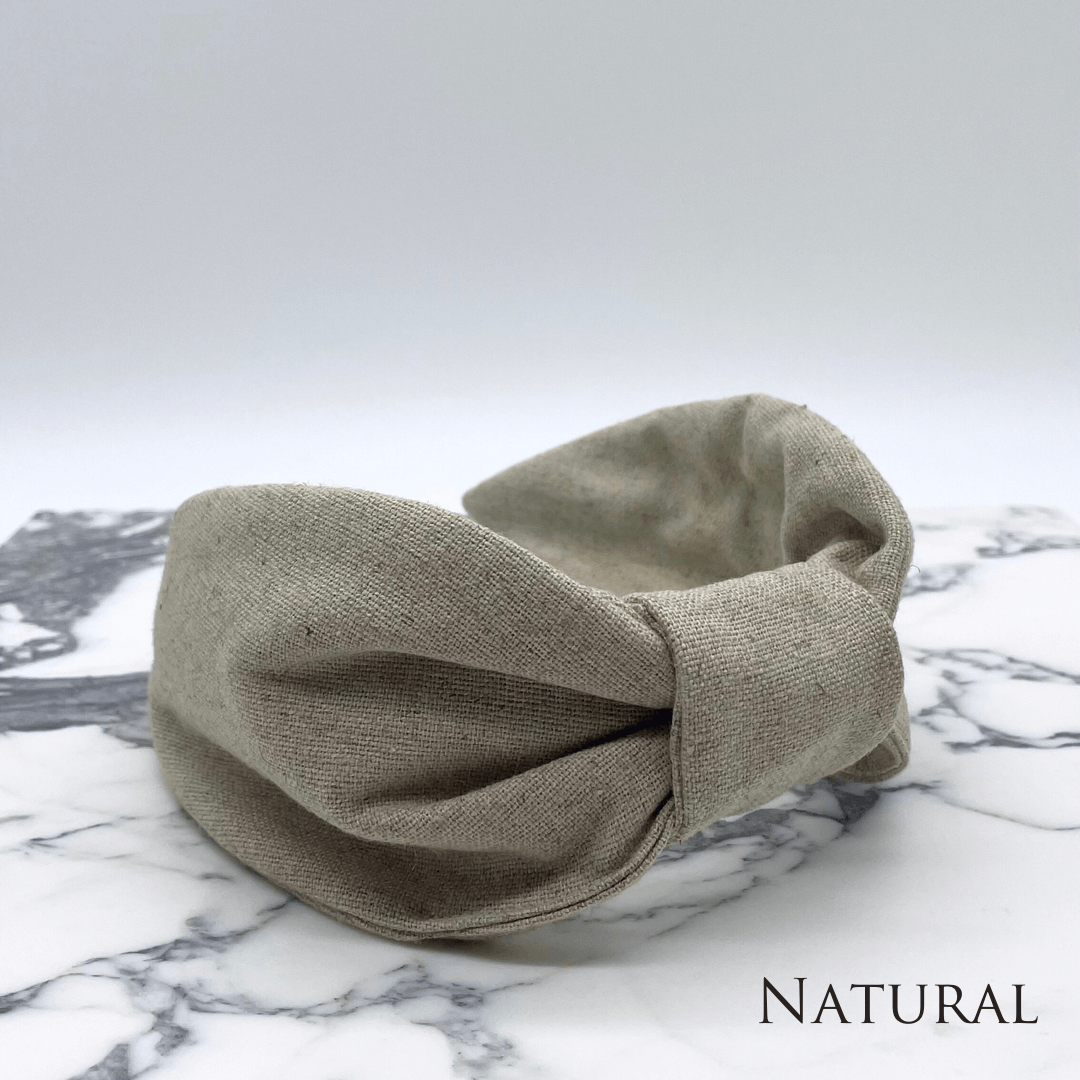 A natural linen knotted headband sitting on a marble tile.