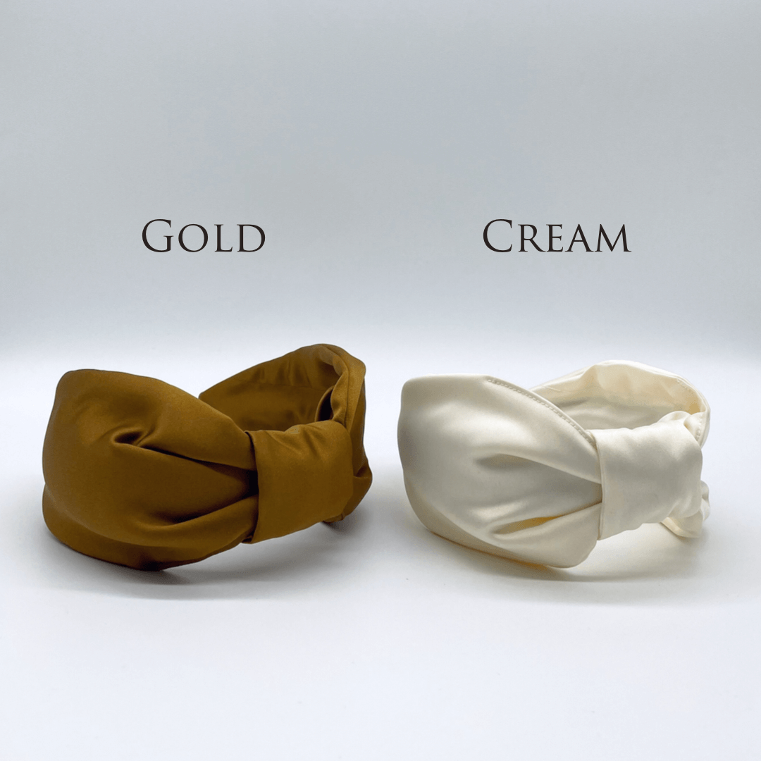 Two satin knot headbands in gold and cream.