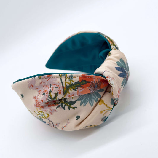 A cream floral knotted headband with a teal satin lining on a white background