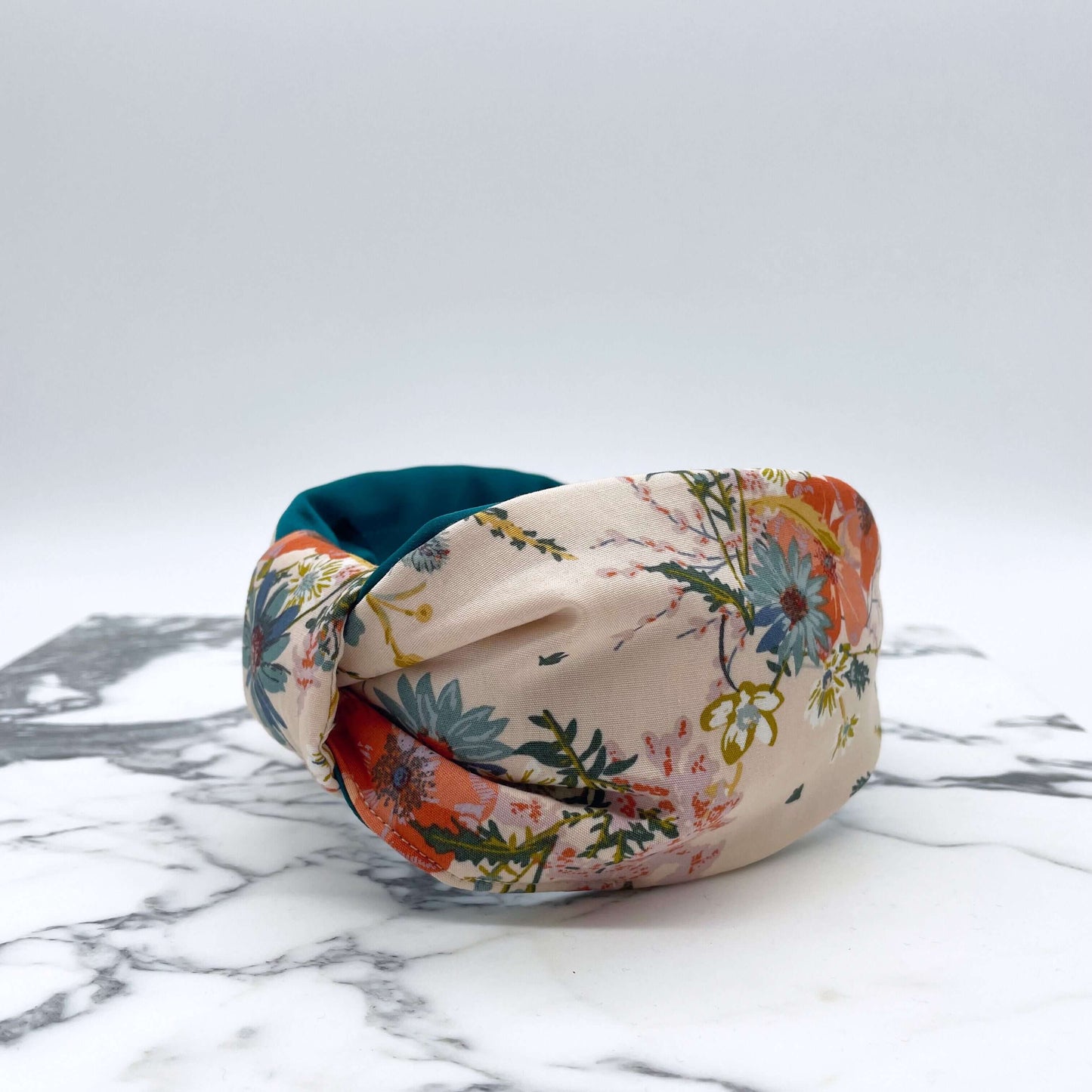 A cream floral knotted headband with a teal satin lining on a marble slab.