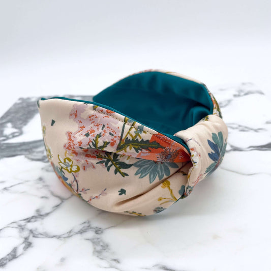 A cream floral knotted headband with a teal satin lining on a marble slab.
