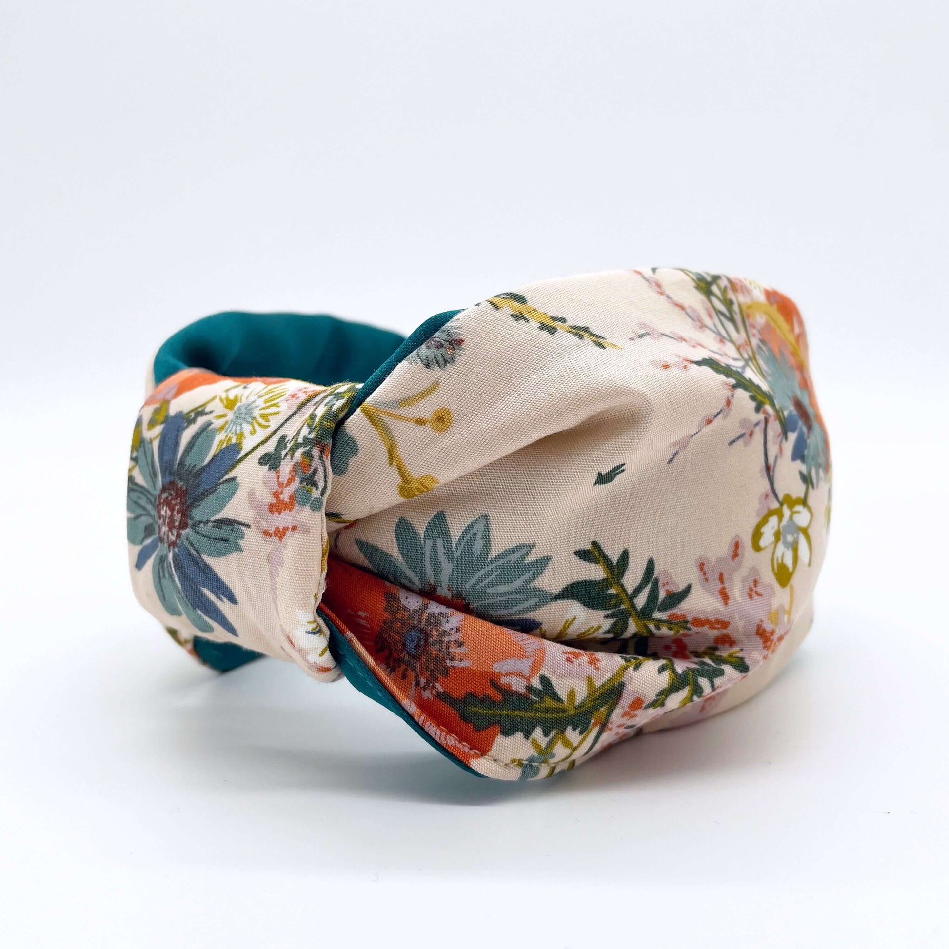 A cream floral knotted headband with a teal satin lining on a white background