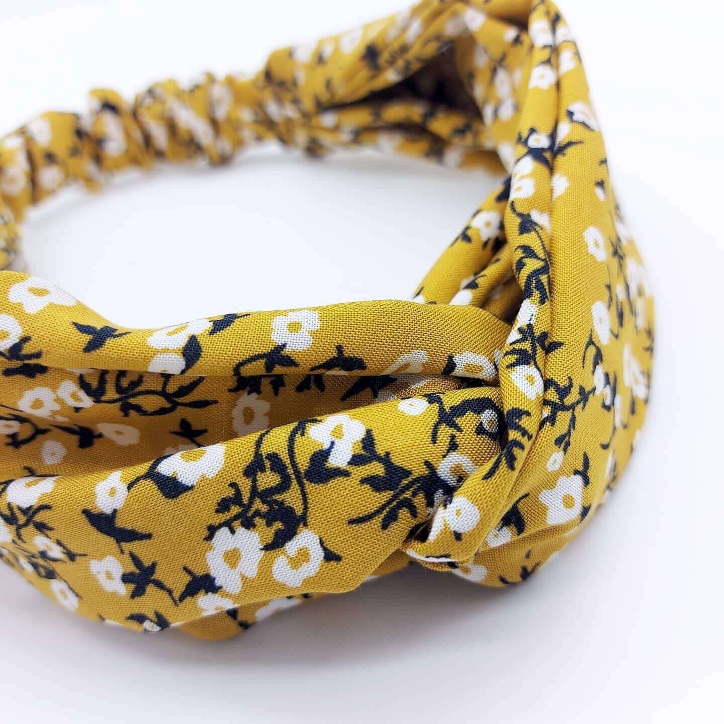A soft, mustard yellow, ditsy print floral turban twist headband with an elasticated panel at the back.