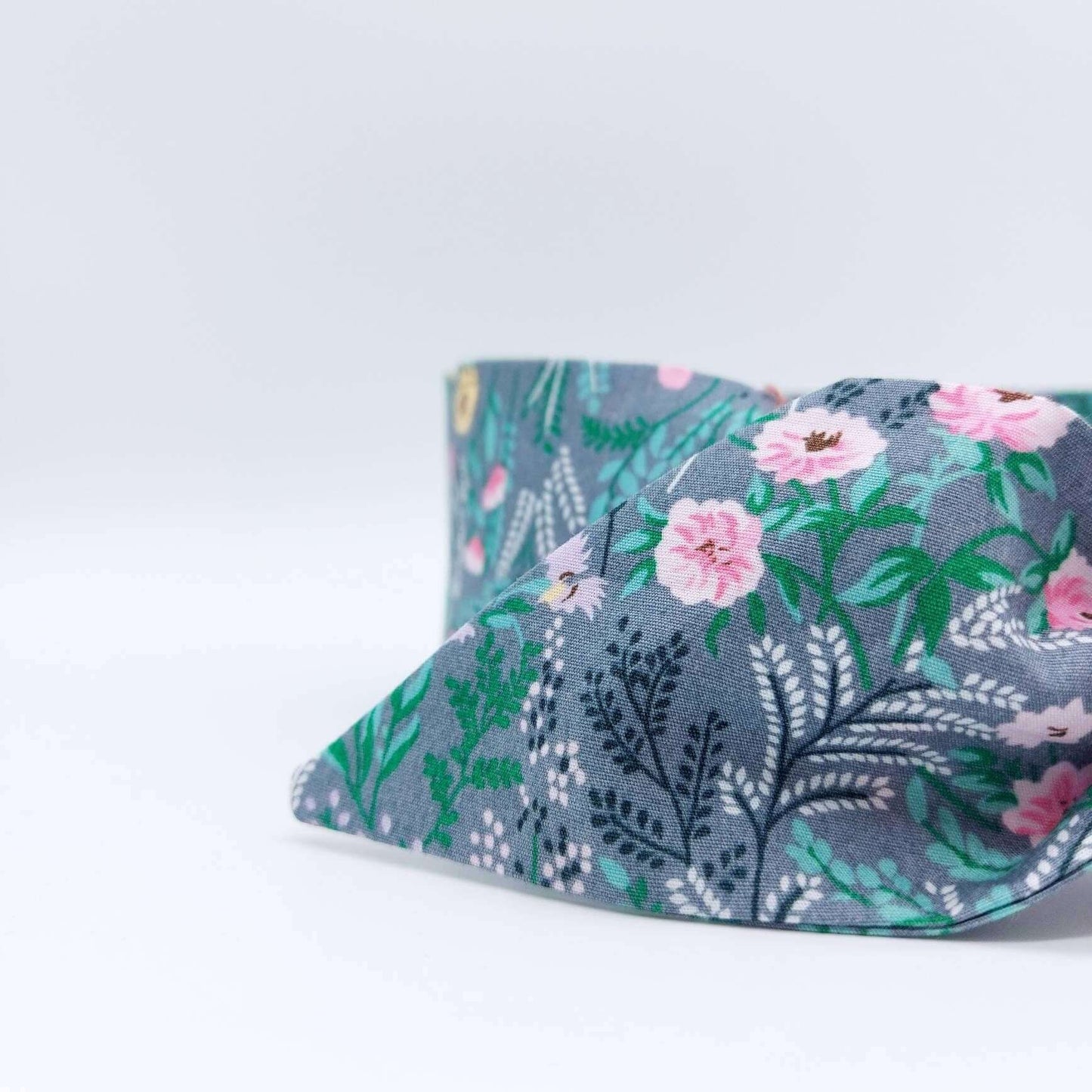 A summery, pale grey, ditsy floral cotton headscarf with tiny pink and green flowers, tied in a pretty knot..