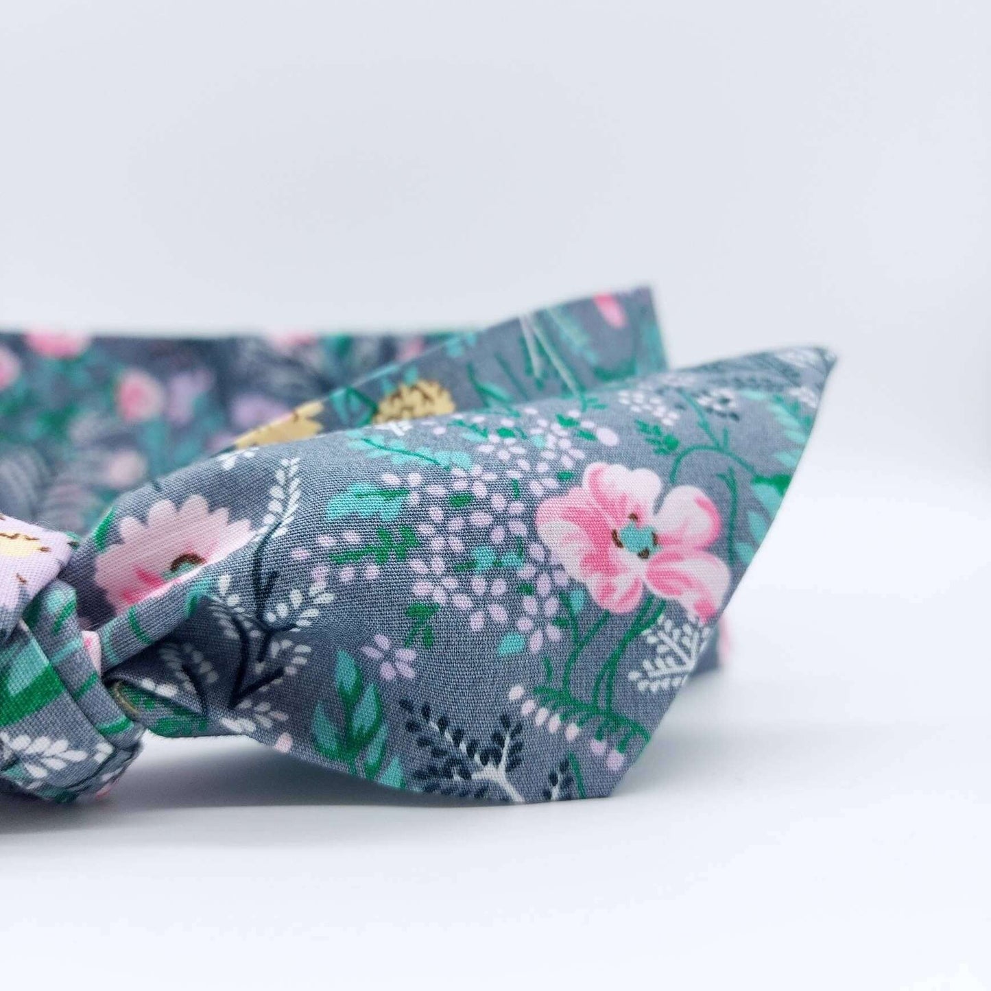 A summery, pale grey, ditsy floral cotton headscarf with tiny pink and green flowers, tied in a pretty knot.