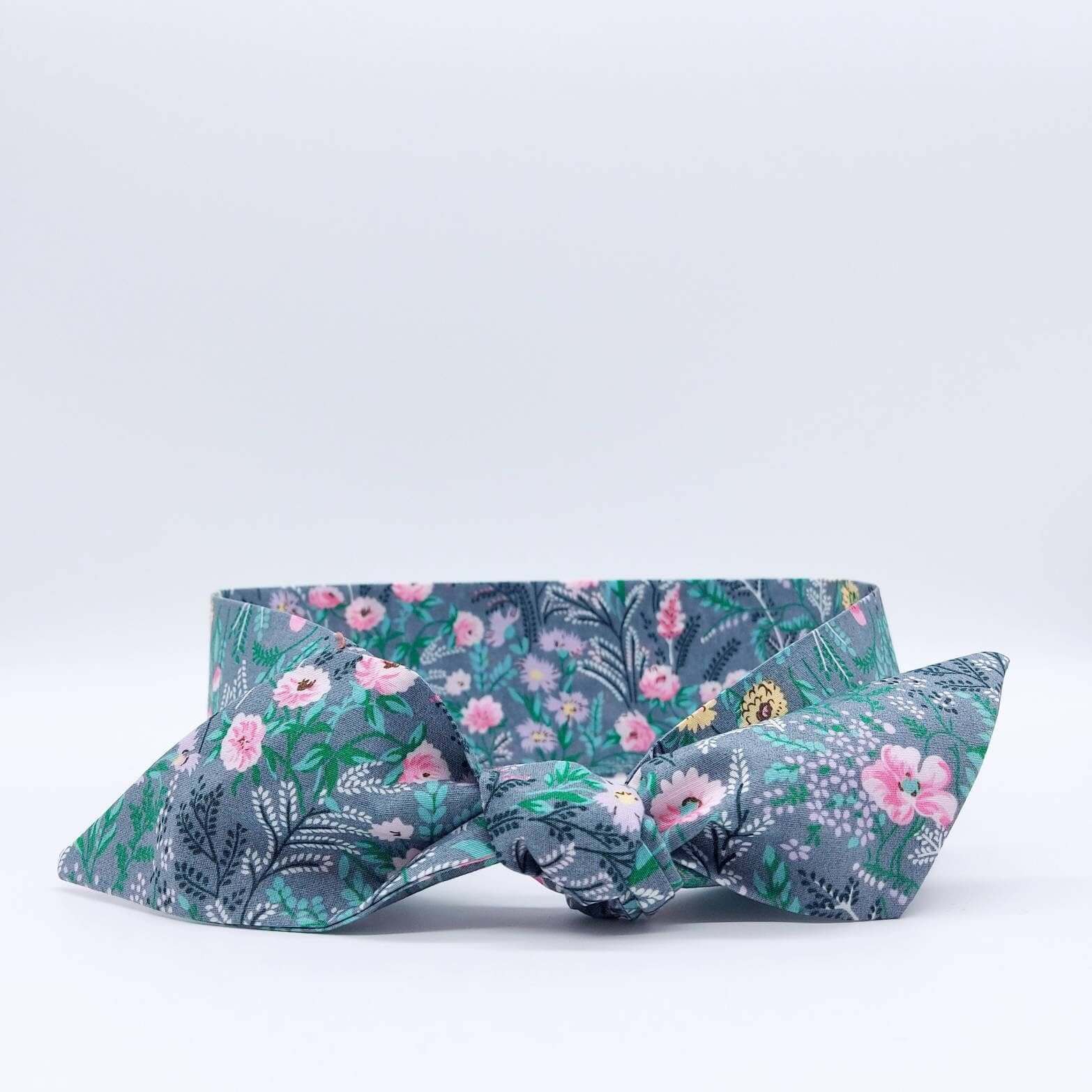 A summery, pale grey, ditsy floral cotton headscarf with tiny pink and green flowers, tied in a pretty knot..