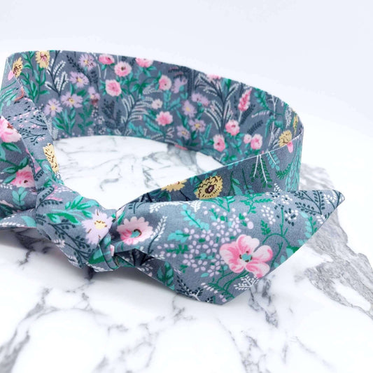 A summery, pale grey, ditsy floral cotton headscarf with tiny pink and green flowers, tied in a pretty knot..