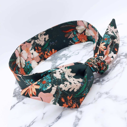 A dark green, floral cotton headscarf with pale pink, blue and orange flowers, tied in a pretty knot.