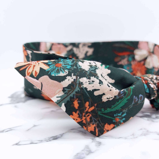 A dark green, floral cotton headscarf with pale pink, blue and orange flowers, tied in a pretty knot.