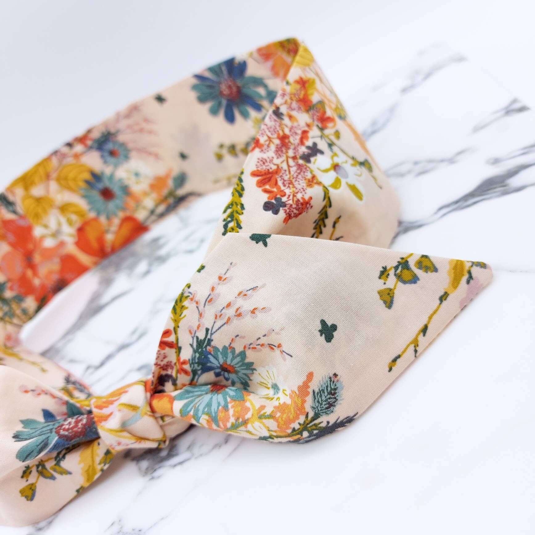 A summery cream, floral cotton headscarf with blue and orange flowers, tied in a pretty knot.