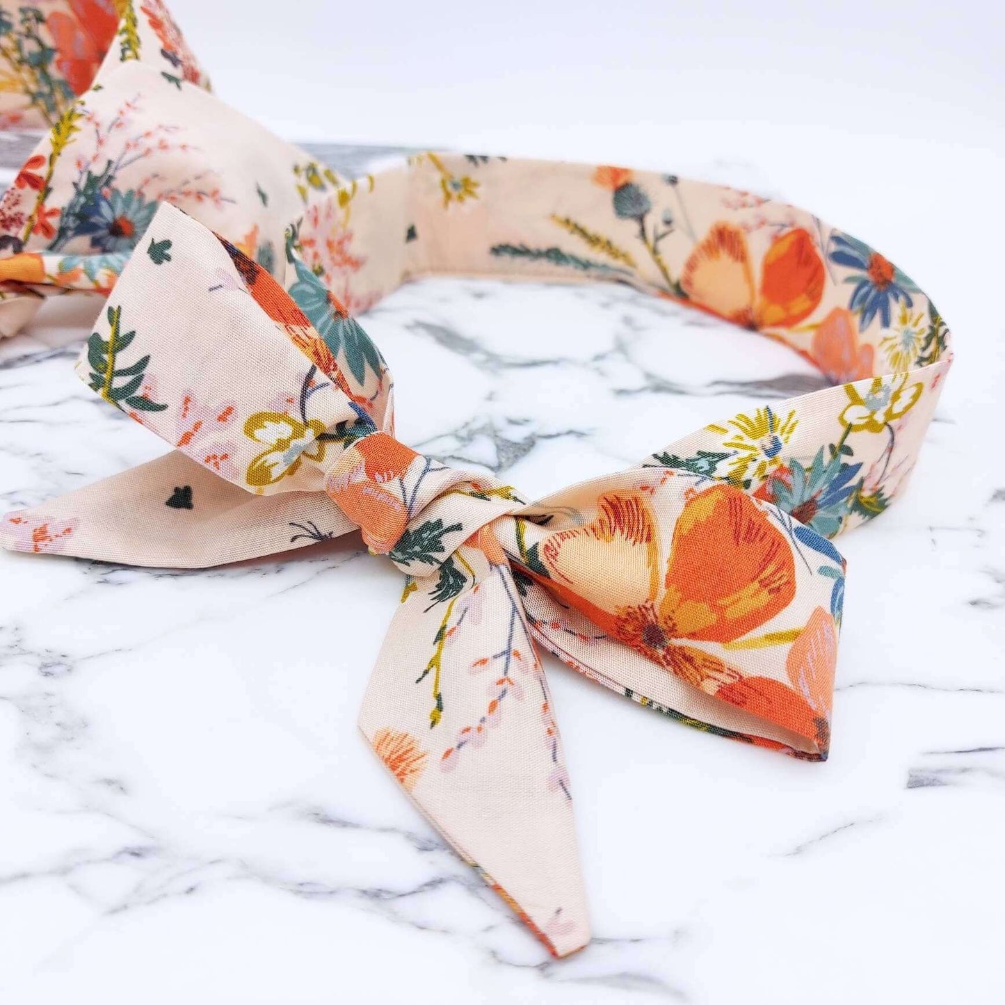 A summery cream, floral cotton headscarf with blue and orange flowers, tied in a pretty bow.