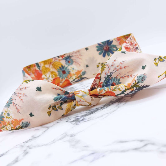 A summery cream, floral cotton headscarf with blue and orange flowers, tied in a pretty knot.