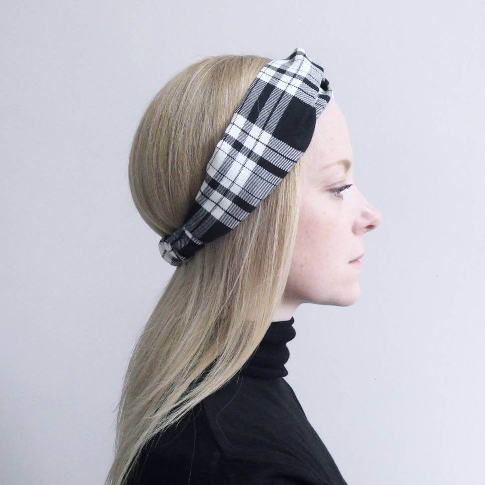 A model wears a soft, black and white tartan plaid check, turban twist headband with an elasticated panel at the back.