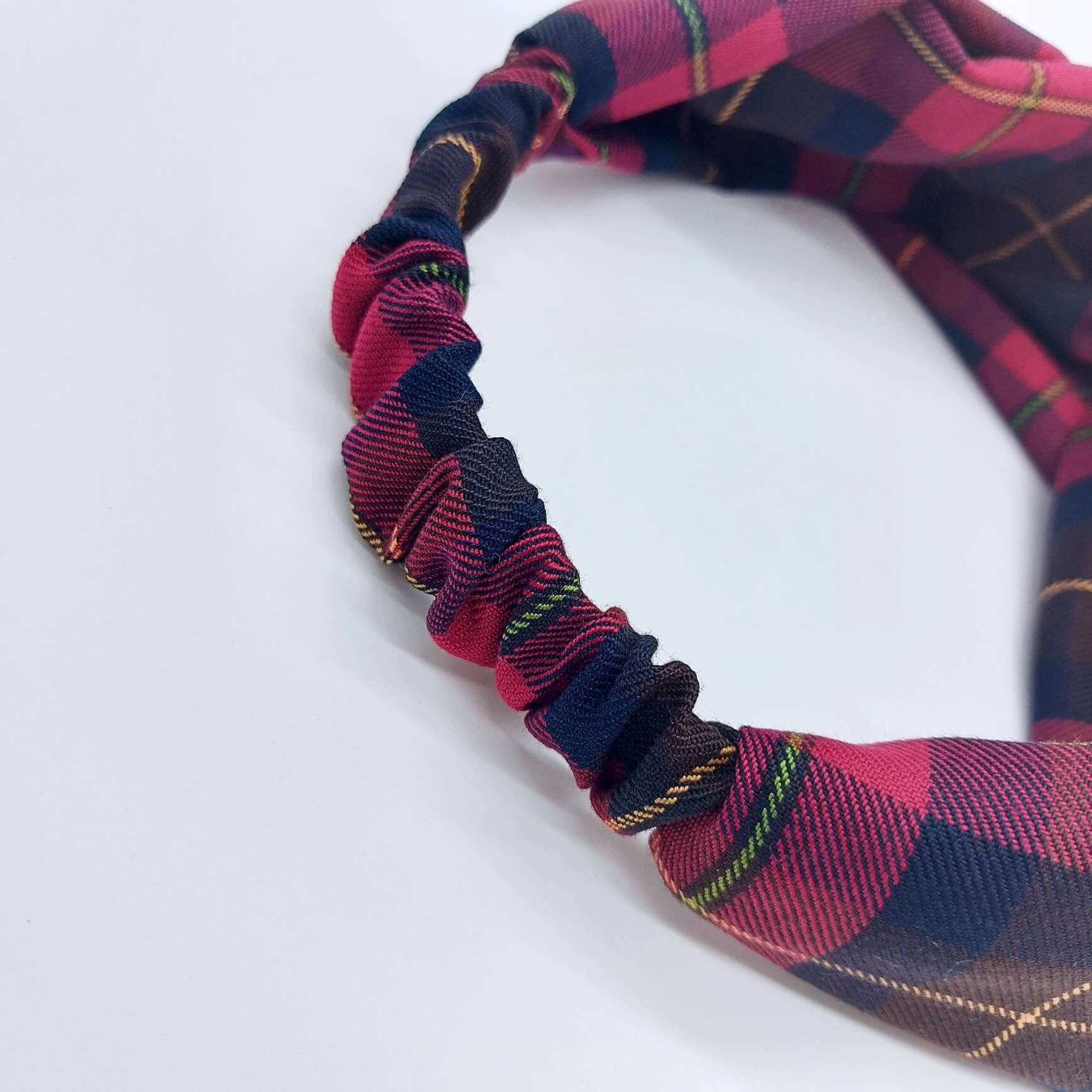 A soft, cranberry red, tartan, plaid, check, elasticated fabric headband, with a turban twist design at the front.