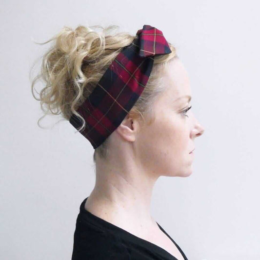 Model wears a dark cranberry and brown fabric, tartan paid tie headscarf, tied in a pretty knot.