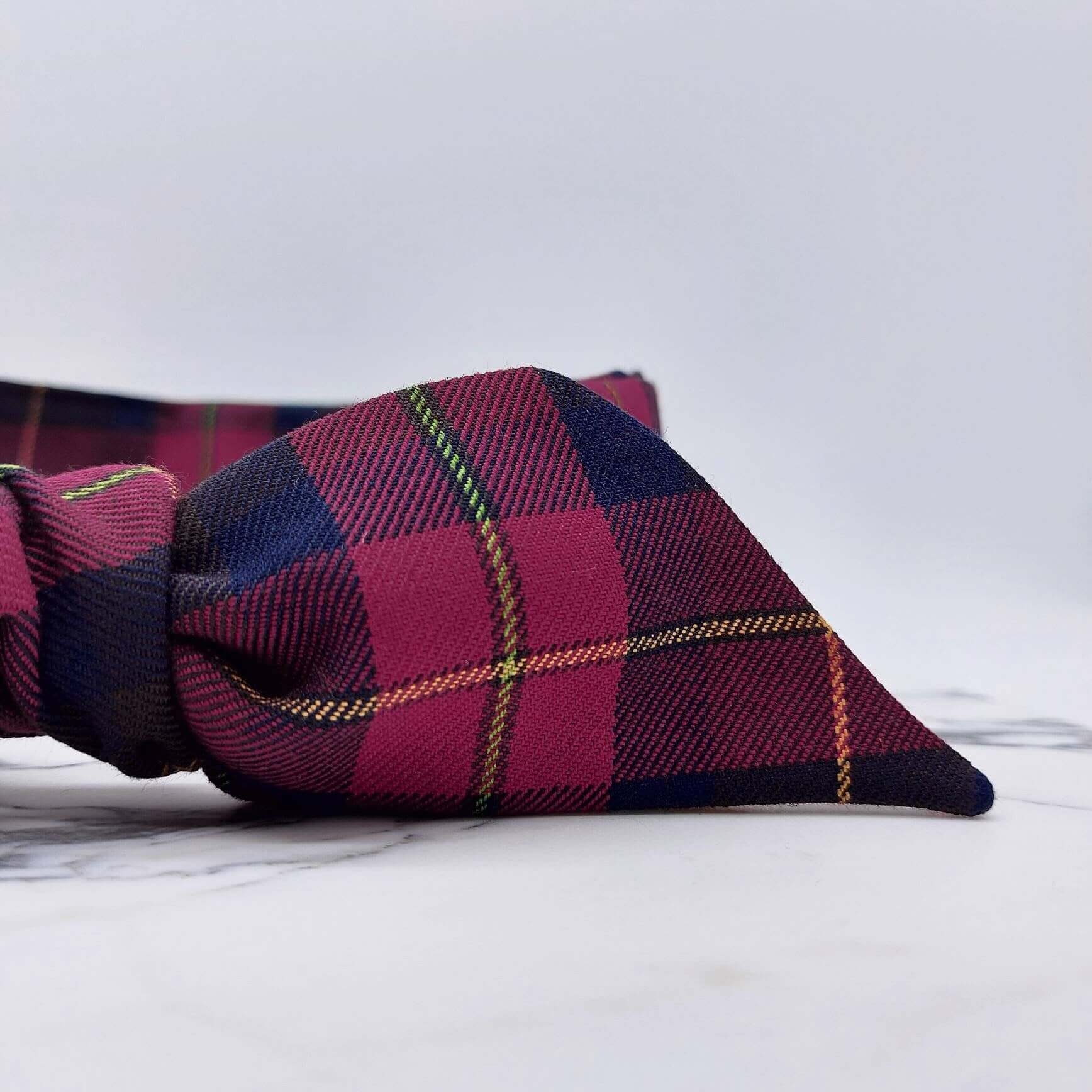 A dark cranberry and brown fabric, tartan paid tie headscarf, tied in a pretty knot.