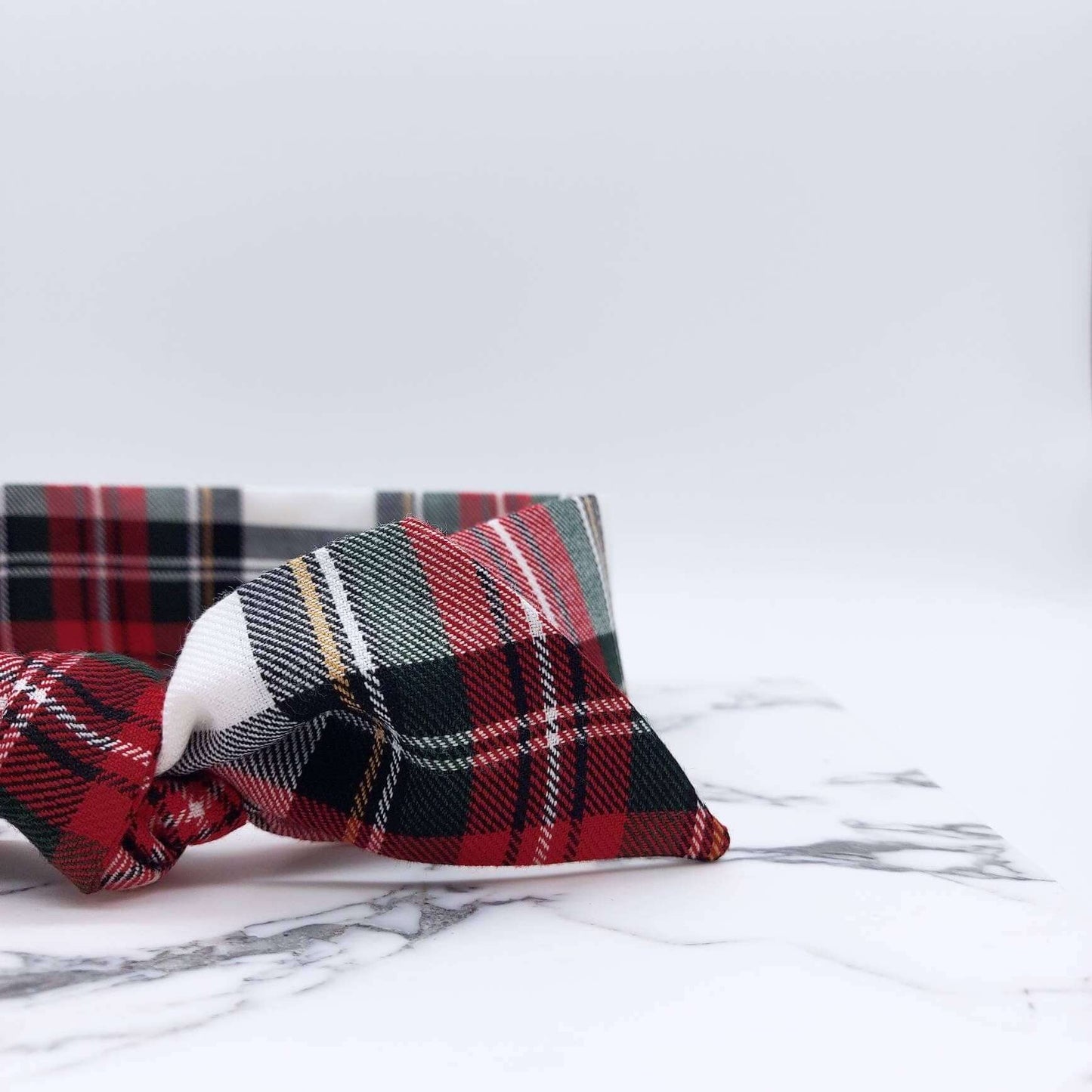 A soft, red and white tartan check fabric, tie headband, tied in a pretty knot.