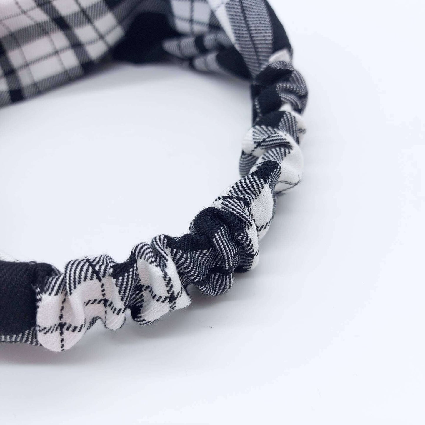 A soft, black and white tartan plaid check, turban twist headband with an elasticated panel at the back.