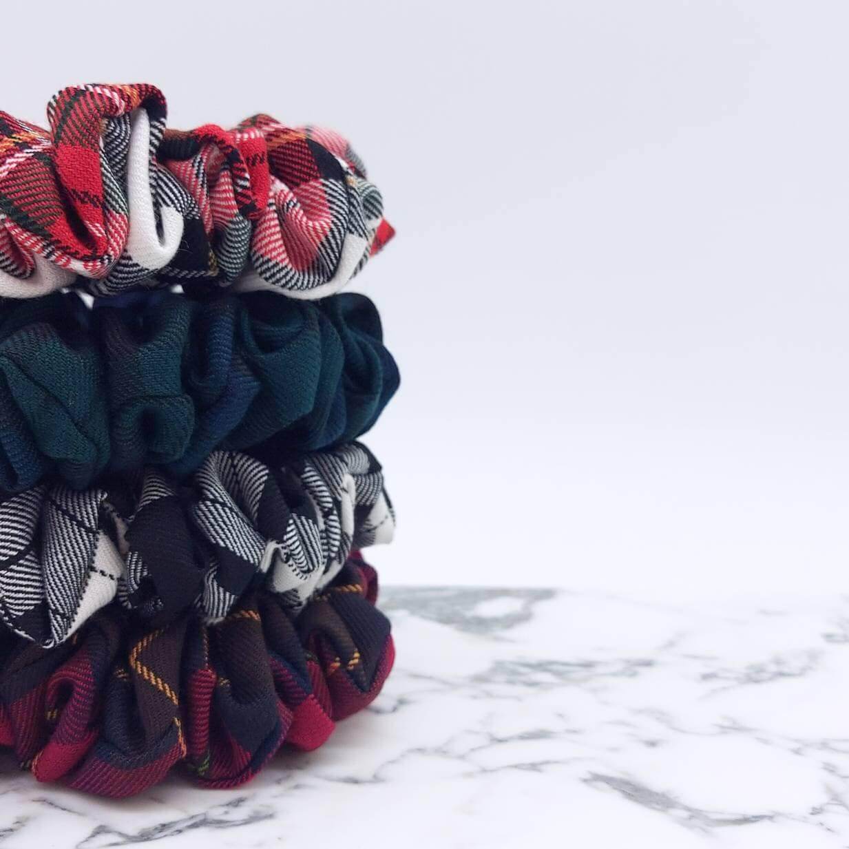 A tower of four, luxury tartan plaid hair scrunchies in red, white, green, navy and cranberry.