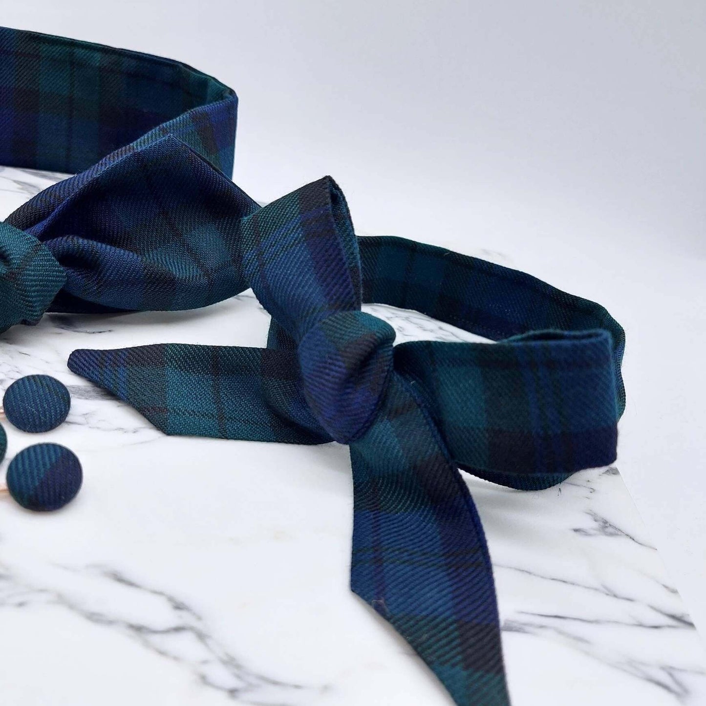 A black and navy blue tartan check fabric, tie headband, tied in a pretty bow.