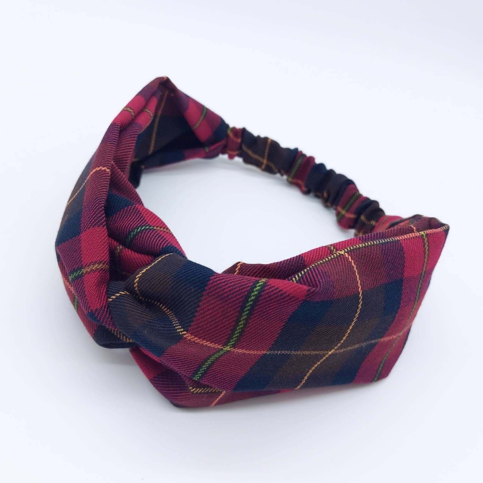 A soft, cranberry red, tartan, plaid, check, elasticated fabric headband, with a turban twist design at the front.