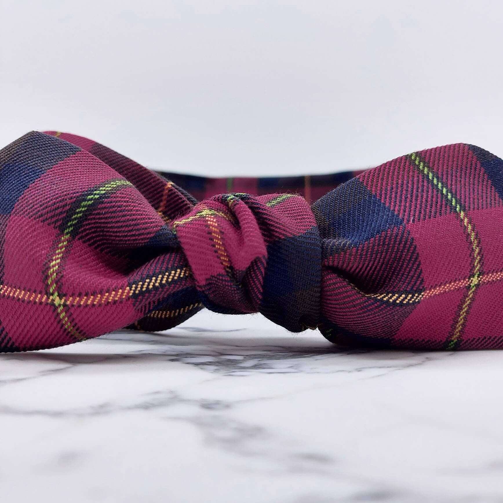A dark cranberry and brown fabric, tartan paid tie headscarf, tied in a pretty knot.