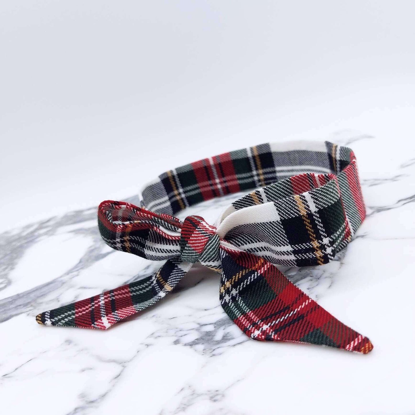 A soft, red and white tartan check fabric, tie headband, tied in a pretty bow.