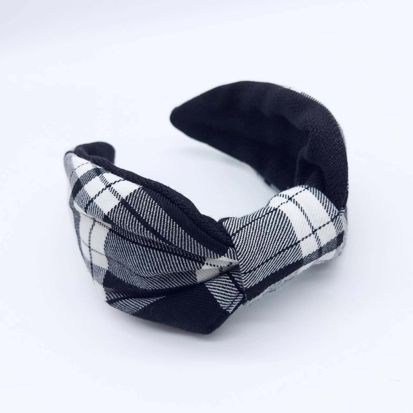 A bow-style, black and white,  tartan plaid fabric headband with plain black lining underneath.