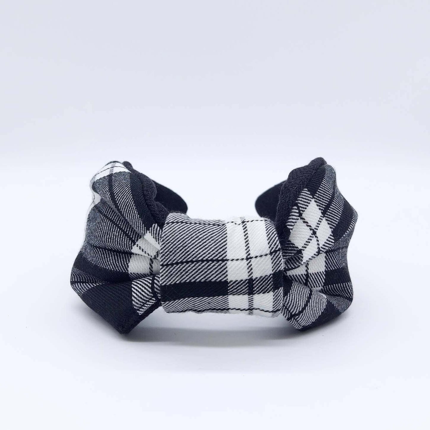 A bow-style, black and white, tartan plaid fabric headband with plain black lining underneath.