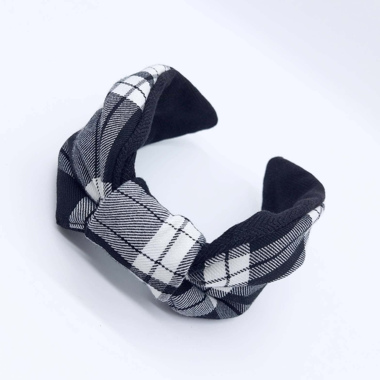 A bow-style, black and white, tartan plaid fabric headband with plain black lining underneath.