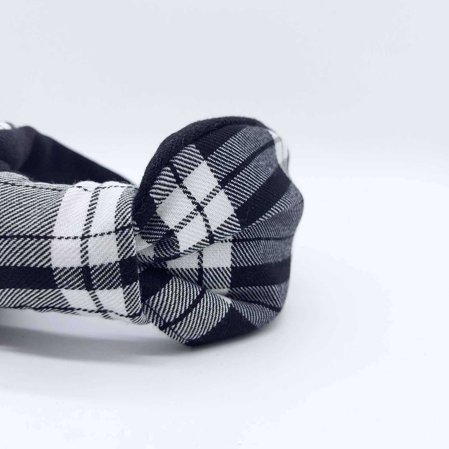 A bow-style, black and white, tartan plaid fabric headband with plain black lining underneath.