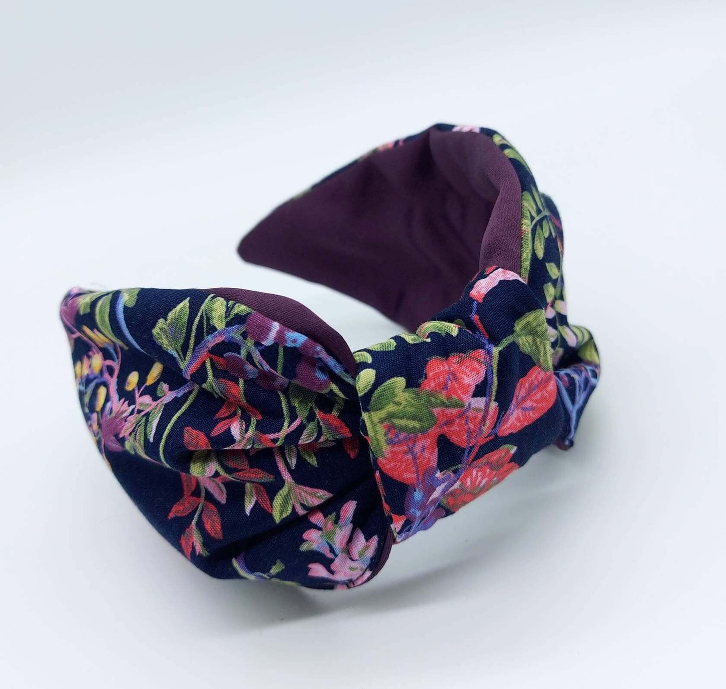 A bow-style, navy blue, red, purple and green floral fabric knot headband with purple satin lining underneath.